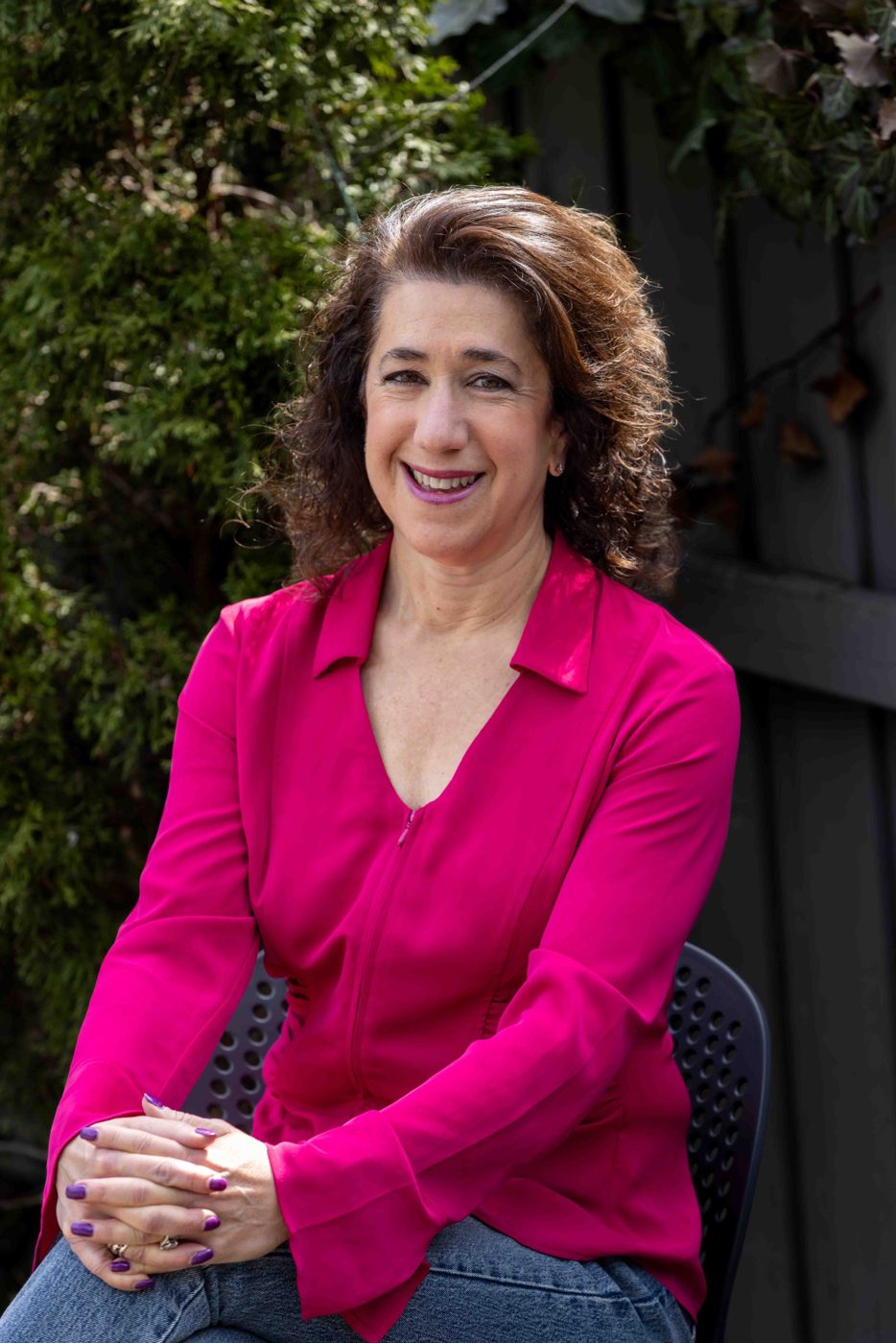 Sara Curwen seated outdoors, hands clasped, smiling